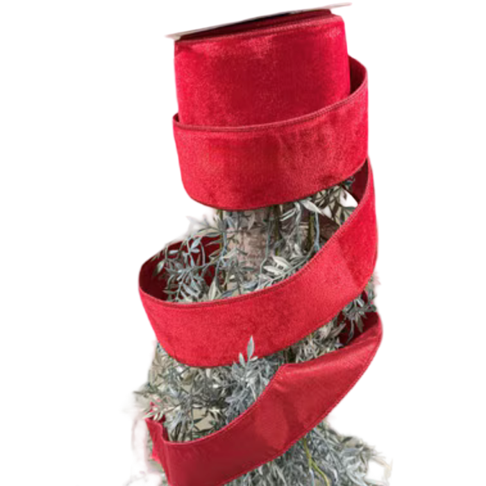 Close-up of JME 2.5-inch red velvet ribbon with matching red edges, loosely wrapped around a spool above decorative greenery.