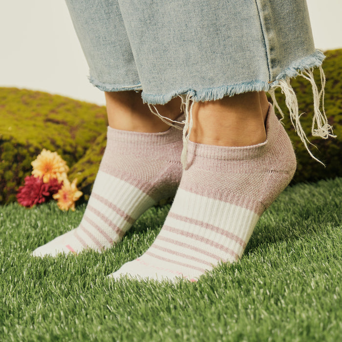 Ankle compression socks with a pink and white contrast stripe design, worn with frayed denim jeans on grass.