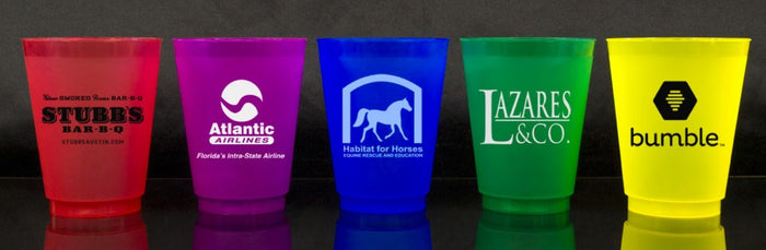 A row of five colorful plastic cups with various logos and text on them, including "STUBBS BAR-B-Q", "Atlantic Airlines", "Habitat for Horses", "L&CO", and "bumble".