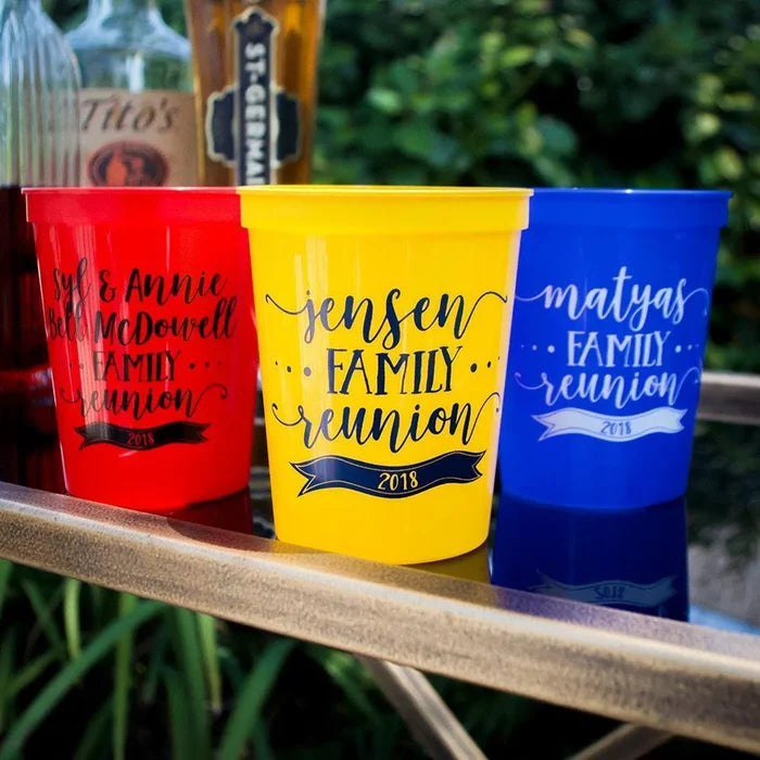 Three colorful plastic cups with personalized text, placed on a table with a blurred background.