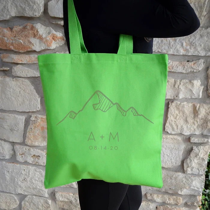A person is holding a lime green tote bag with a mountain graphic and text on it.