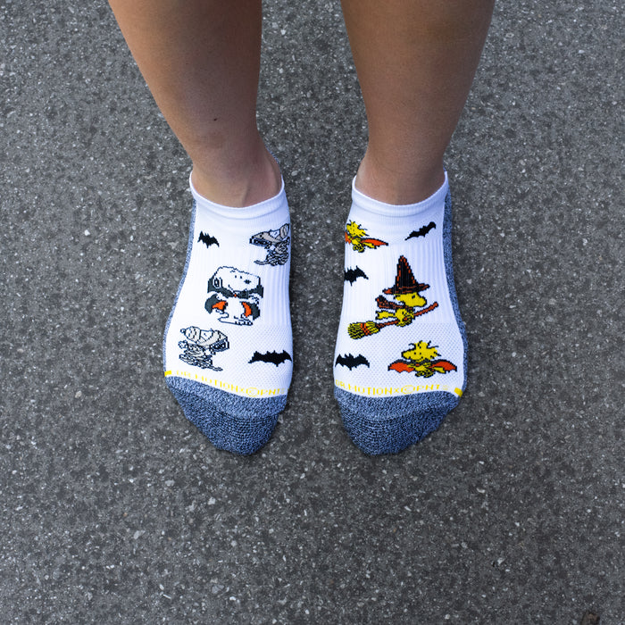 White and black marled ankle compression socks with Peanuts Halloween designs, worn in a lifestyle setting.