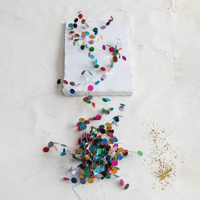 Multicolored holographic confetti garland with small reflective circular accents along a slender strand, shown vertically against a white background.