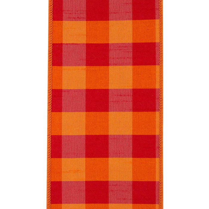 A close-up of a woven textile with a bold plaid pattern in red, orange, and pink, finished with a decorative braided border on the left side.