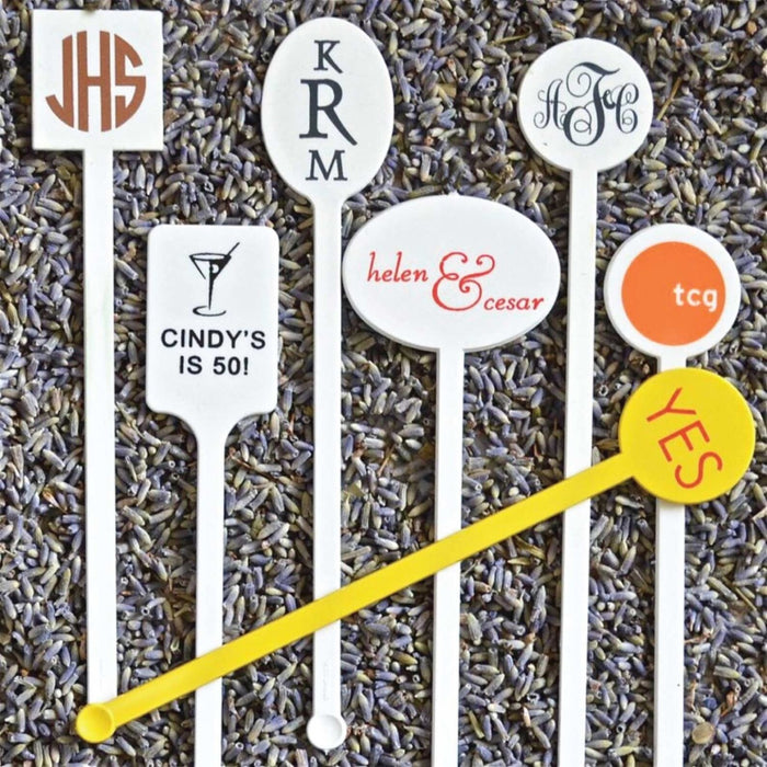 a collection of personalized cocktail stirrers, each with a unique monogram or text design.