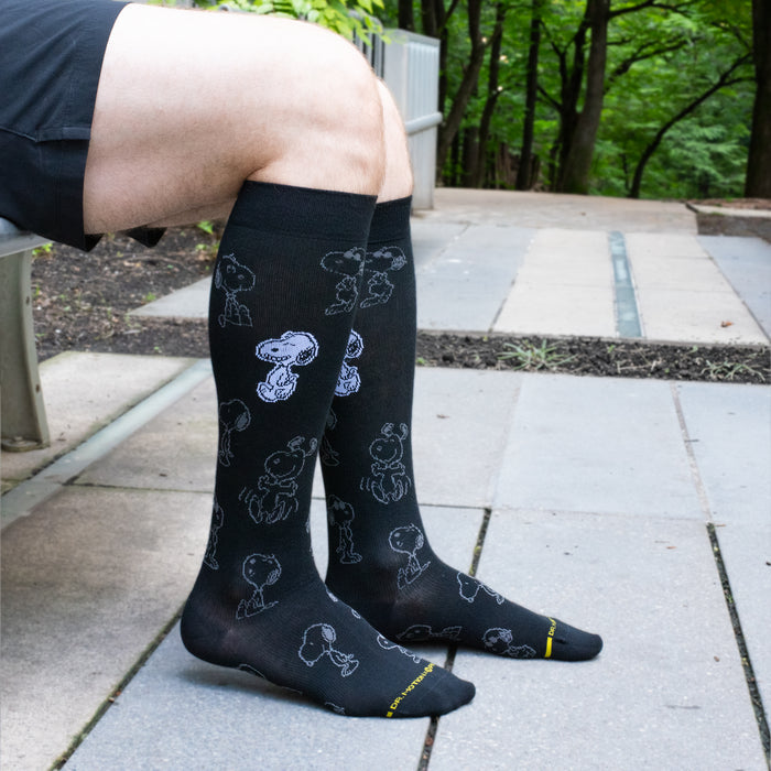 Black knee-high compression socks for men with a pop-art Snoopy design, worn in a lifestyle setting.