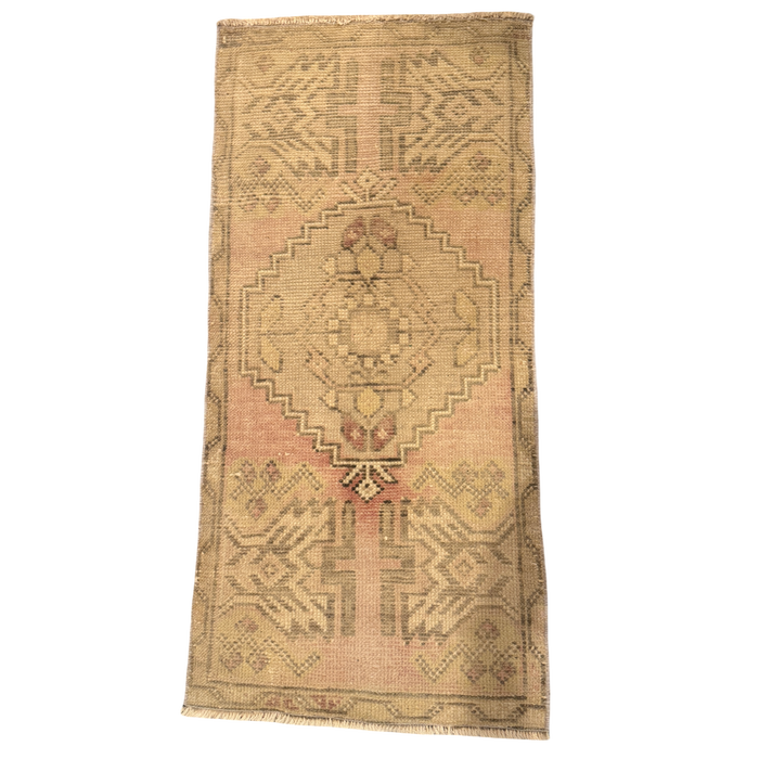 Narrow mini rug with a blush pink and golden beige ground, muted olive geometric medallion, patterned border, and short cream fringe.