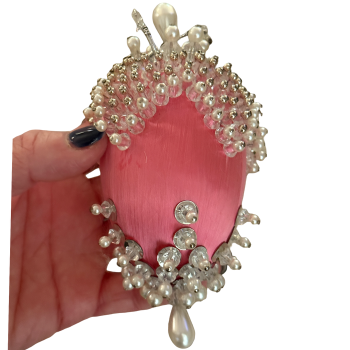 Close-up of clear beads, pearl-look accents, and loose threads on a vintage pink satin ornament.